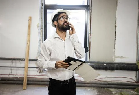 Engineer in hardhat using phone and holding tablet Stock-Fotos