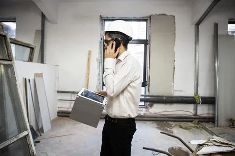 Engineer in hardhat using phone and holding tablet Stock Photos
