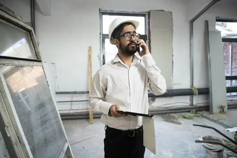 Engineer in hardhat using phone and holding tablet Фото