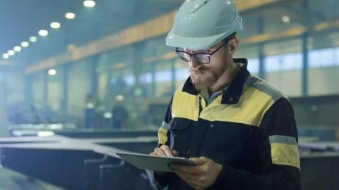 Engineer in hardhat is using a tablet computer in a heavy industry factory. Stock Photos