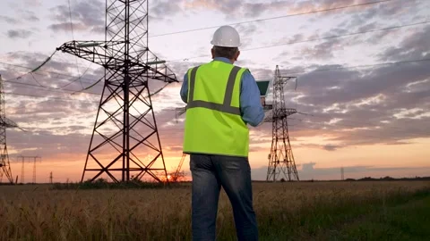 Engineer in helmet holds tablet walking against power transmission lines Stock Footage 248590352