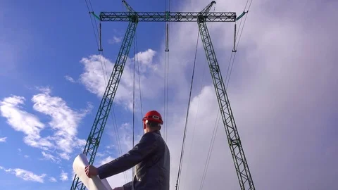 Engineer in a helmet with a technical plan stands under the power lines Stock Footage 77699652