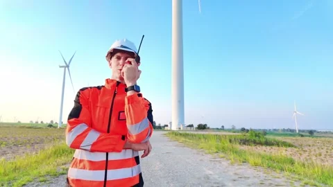 Engineer in high-visibility gear using a radio at a wind farm Stock-Footage 329953892