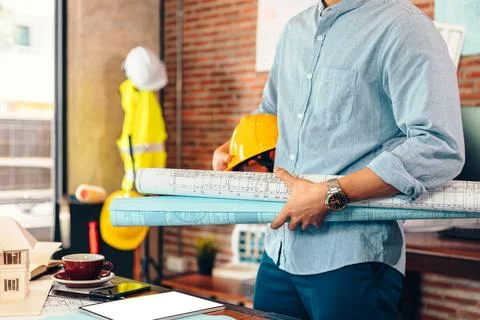 Engineer hold engineer drawing design blueprints and safety helmet in room .. Stock Photos