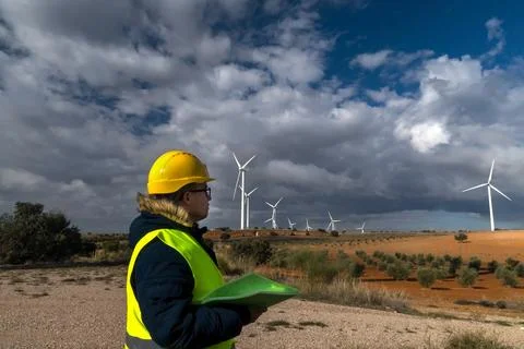 Engineer holding blueprints inspecting a wind farm under a cloudy sky Stock Photos