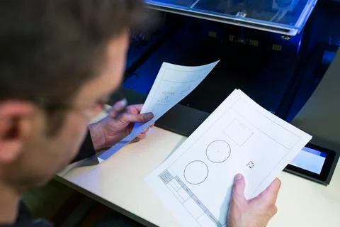 Engineer holding documents by 3D printer at table in office Stock Photos