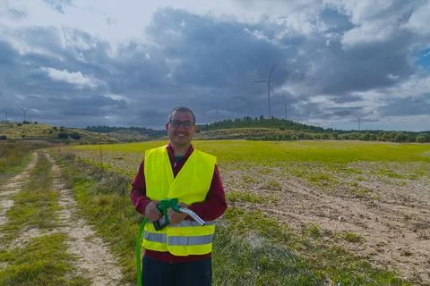 Engineer holding fuel nozzle in front of wind turbines and cloudy sky Stock Photos