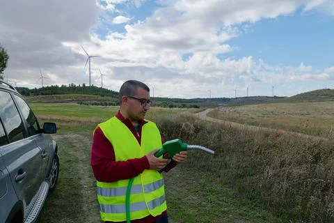 Engineer holding fuel nozzle looking at wind turbines in field with cloudy sk Stock Photos