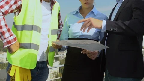 Engineer holding house scheme, discussing plan with female architect and builder Stock-Footage 117195487