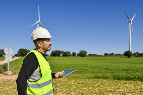 Engineer holding tablet and inspecting wind turbines in green field Stock Photos
