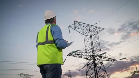 Engineer inputs data on tablet and nods head by power transmission lines support Stock Footage 254925257