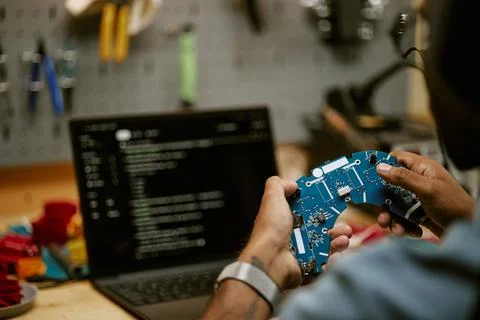 Engineer Inspecting Circuit Board in Front of Laptop Stock Photos