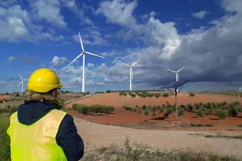 Engineer inspecting wind turbines and solar panel in rural landscape Stock Photos