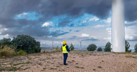 Engineer inspecting wind turbines in a wind farm under cloudy sky Stock Photos