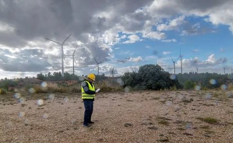 Engineer inspecting wind turbines in a wind farm under cloudy sky Stock Photos