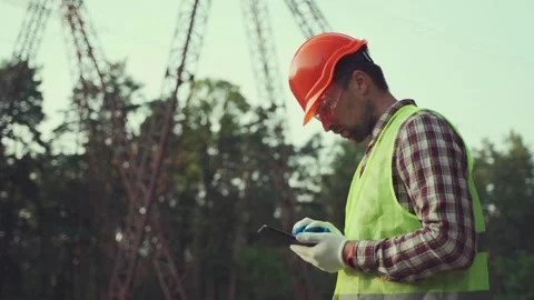 Engineer inspects high-voltage power lines, using tablet for calculations and Video stock 290524783