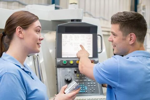 Engineer Instructing Female Apprentice On Use Of CNC Machine Foto stock