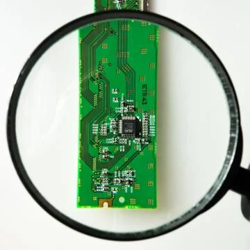 Engineer looking at a circuit board through a magnifying glass 스톡 사진