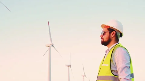 Engineer looking at wind turbines and putting a white helmet. Safety first Stock Footage 246380258