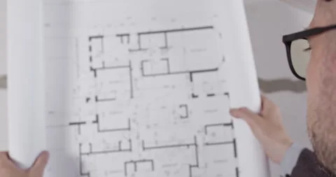 Engineer looks at paper floor plan of building standing in hall Stockbeeldmateriaal 309929706