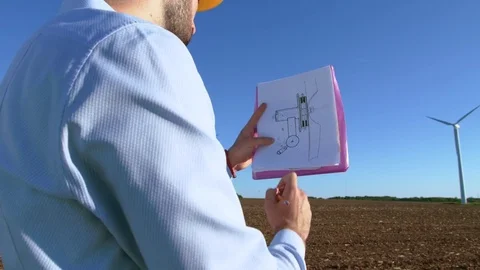 Engineer looks at the windmill drawings on the background of a windmill and Stock-Footage 76549667