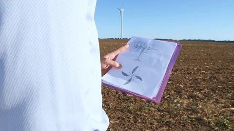Engineer looks at the windmill drawings on the background of a windmill. Video stock 76570609