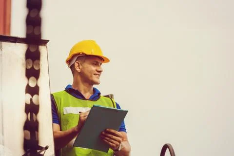 Engineer man in hard hat and safety vest standing on container stackers contr Фото