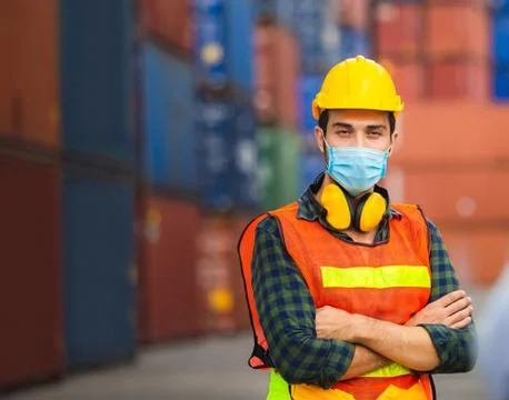 Engineer man in hard hat wearing protection face mask with arms crossed at cargo 写真素材