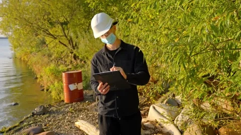 Engineer with Mask Taking Notes During Environmental Inspection by River Stock Footage 321865215