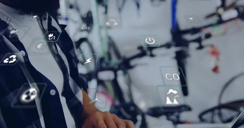 Engineer observing floating energy icons in bike shop and typing on laptop Stock Footage 328507701