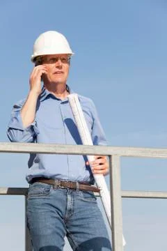 Engineer or architect with hard hat and blueprint in his hand on a constructi Stock Photos