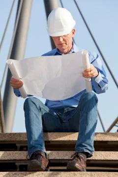 Engineer or architect with hard hat reading a plan while sitting in front of  Stock Photos