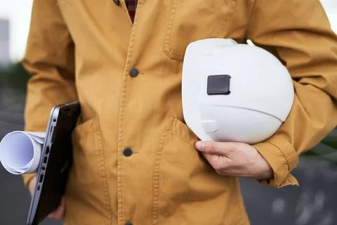 Engineer in orange jacket with hardhat, laptop and blueprint 库存照片