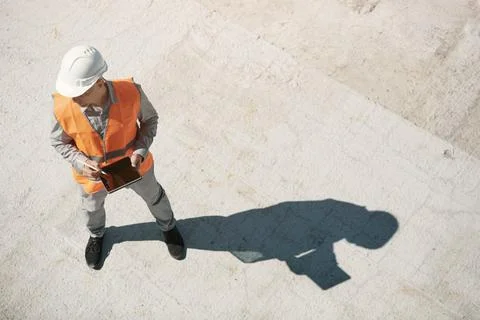 An engineer in an orange vest and a white construction control helmet conduct Stock Photos