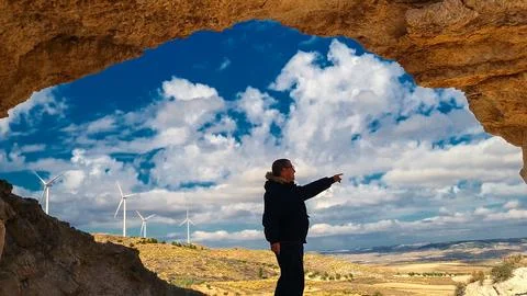 Engineer pointing at wind turbines from a cave: promoting renewable energy Stock Photos