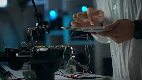 Engineer programming a robotic device in a modern laboratory during the even 動画素材 323765690