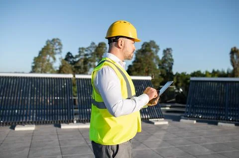 Engineer in protective vest analyzing solar energy installation with gadget 写真素材