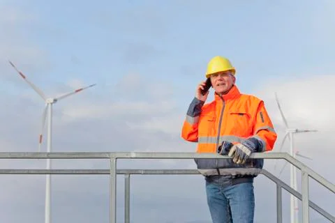 Engineer with protective work wear talking on mobile phone in front of wind t Stock Photos