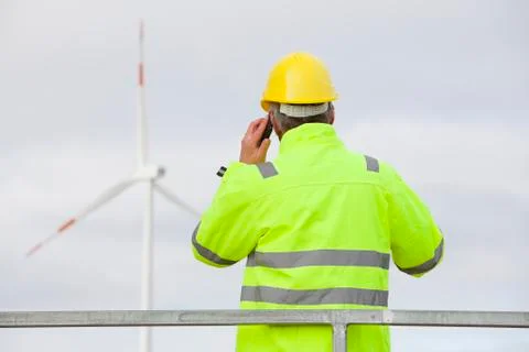 Engineer with protective work wear talking on mobile phone in front of a wind Stock Photos
