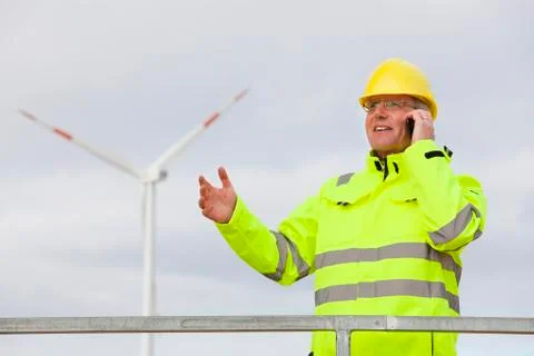 Engineer with protective work wear talking on mobile phone in front of a wind Фото