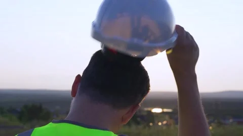 An engineer puts on a helmet at sunset 스톡 동영상 253324730