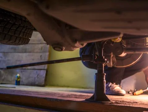 Engineer rapairing car in garage using jack under it Stock Photos