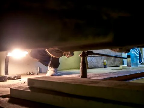 Engineer rapairing car in garage using jack under it Stock Photos