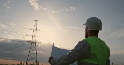 Engineer reads plan near power transmission lines at sunset 動画素材 156916441