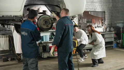 Engineer Repairing Car While Lab Technicians Observe and Take Notes in Workshop Stock Footage 303065718