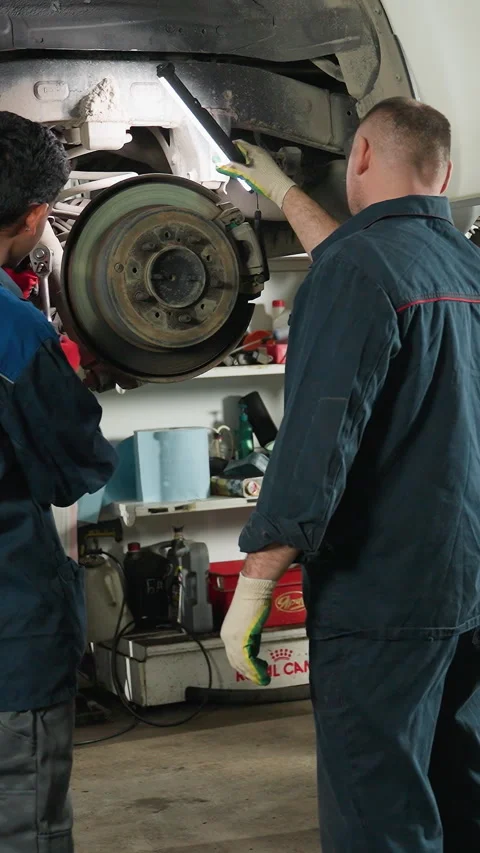 Engineer Repairing Car While Lab Technicians Observe and Take Notes in Workshop Stock Footage 318254013