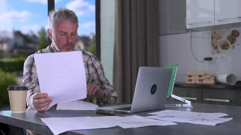Engineer reviewing technical documents at kitchen table with laptop and Stock Footage 334870951