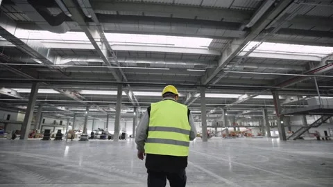 Engineer in safety vest walking through empty industrial factory warehouse. Stock Footage 337518979