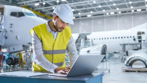 Engineer in Safety vest Working on Computer in Aircraft Maintenance Hangar Foto stock
