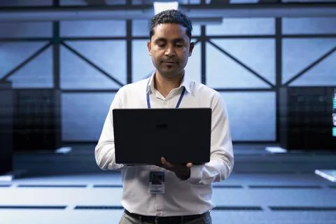 Engineer in server farm checking recovery plan on laptop, monitoring data center Stock Photos